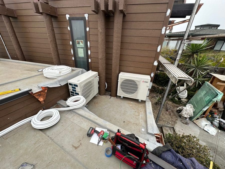 Two Mitsubishi outdoor units with coiled refrigerant line sets during installation on a Watsonville deck