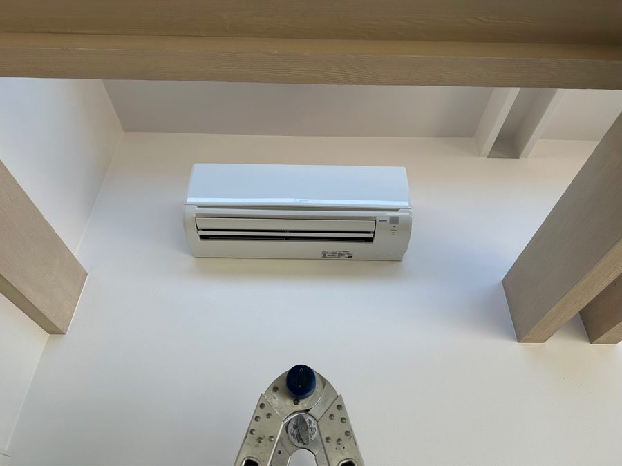 Wall-mounted Mitsubishi ductless indoor head mounted high on a white wall between wood beams, Watsonville, CA